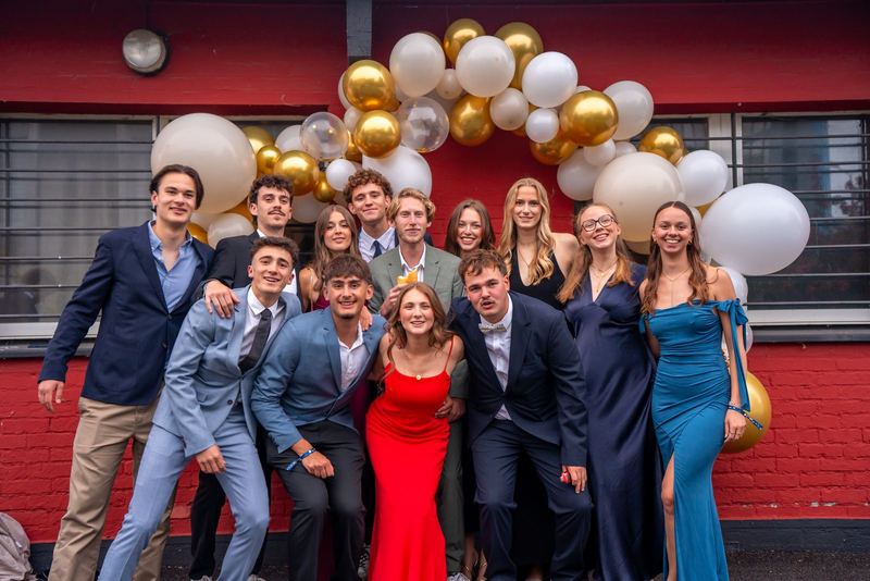 Bal promo 2029, photo de groupe devant une façade rouge sous une arche de ballons dorés