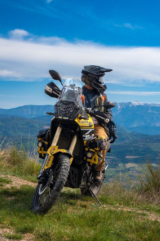 Moto trail en tenue tout-terrain au sommet d'une montagne, panorama de vallée et reliefs enneigés